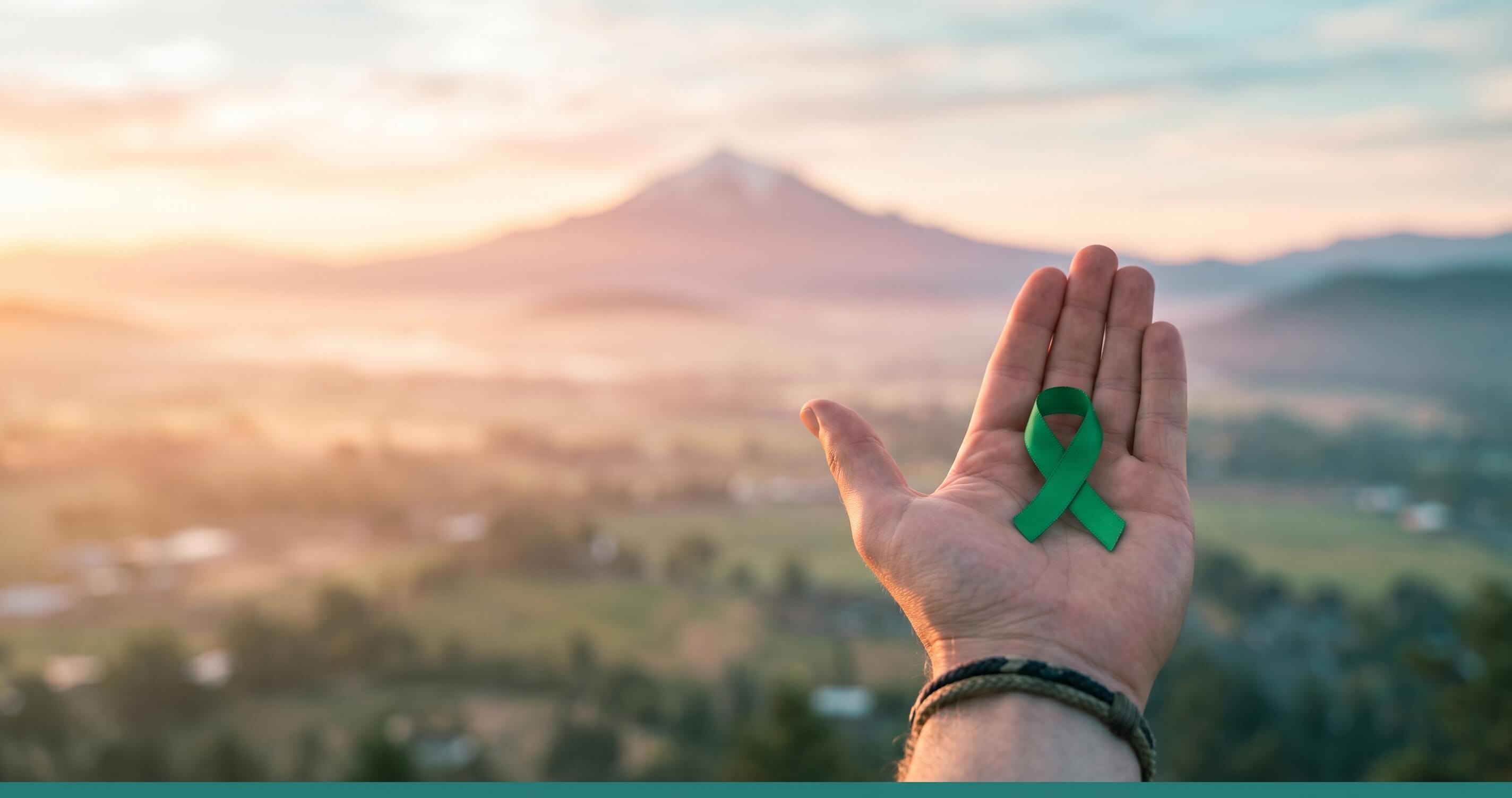 Sunrise over the Rogue Valley with a hand holding a green awareness ribbon